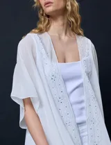 Kimono de gasa color blanco, con diseño abierto y mangas amplias. Presenta detalles de apliques brillantes a lo largo de la abertura frontal.