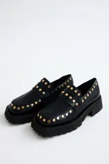 Mocasines negros de cuero con suela track y detalle de tachas doradas.