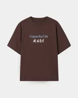 Remera marrón oversize con cuello redondo y mangas cortas. Estampado frontal con el texto "Uruguay Run Club" en celeste y siluetas blancas de personas corriendo.