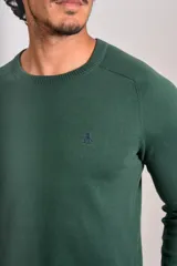 Sweater de punto fino color verde oscuro, con cuello redondo, mangas largas y puños y ruedo acanalados. Presenta un pequeño logo bordado en el pecho.