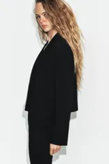 Blazer corto de corte recto con cuello de solapa, manga larga y hombreras. Presenta un diseño minimalista sin botones y forro interior a tono.