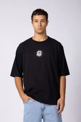 Remera oversize de corte holgado, color blanco, con cuello redondo y mangas cortas. Presenta un pequeño estampado circular en el centro del pecho con un diseño abstracto inspirado en arrecifes.