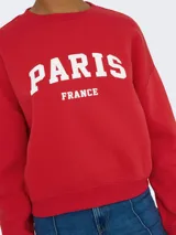 Buzo rojo de manga larga con cuello redondo y puños acanalados. Presenta un fit holgado y un largo corto, con estampado frontal que dice "PARIS FRANCE" en blanco.