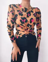Remera de manga larga color beige con estampado animal print en negro y fucsia. Presenta cuello redondo y nudo decorativo en la parte delantera.