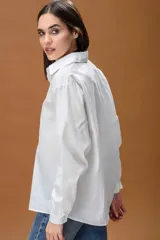 Camisa blanca de corte oversize, con cuello clásico, cierre frontal de botones y mangas largas con puños abotonados.