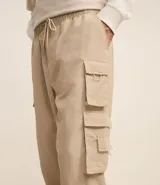 Pantalón jogger color beige, confeccionado en tejido plano de poliamida, con cintura elástica y cordón de ajuste. Presenta múltiples bolsillos cargo con solapa en los laterales y elástico en los puños.