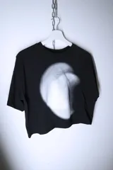Remera negra de corte holgado y diseño cropped, con estampado frontal abstracto en tonos blancos y grises que simula un efecto de luz difusa.