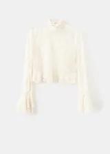 Blusa de encaje color crema con cuello alto, mangas largas con volados en los puños y detalle de volado en el ruedo.
