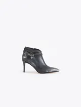 Bota corta de cuero vacuno color negro con acabado metalizado, taco fino mediano y punta fina. Presenta una tira decorativa con hebilla metálica y un dije en forma de corazón. Cuenta con cierre lateral para un calce cómodo y está completamente forrada en cuero.