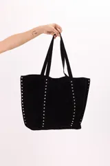 Bolso tipo tote amplio confeccionado en símil gamuza, color negro, con detalle de tachas metálicas plateadas en el frente y laterales. Cuenta con doble asa de hombro.