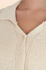 Sueter de punto color beige, con cuello polo, cierre frontal con botones y mangas largas con puños acanalados.