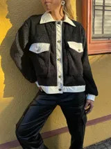 Campera de corderito negra con cuello, solapa, puños y bolsillos de cuero sintético color crema.