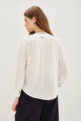 Camisa blanca de manga larga con cuello mao y cierre frontal de botones. Presenta delicados bordados florales en tonos neutros a lo largo de la parte frontal y en los hombros.