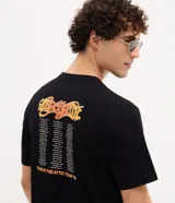 Remera negra de algodón con estampado localizado de la banda Aerosmith en tonos naranja y amarillo. Presenta cuello redondo y manga corta.