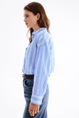 Camisa oversize confeccionada en mezcla de lino y viscosa, con diseño a rayas verticales en tonos celeste y blanco. Cuenta con cuello clásico, cierre frontal de botones, hombros caídos y mangas largas con puños abotonados.