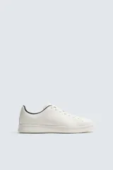 Zapatilla de cordones confeccionada en piel, con horma redonda y suela a tono. Presenta un diseño minimalista con detalle de contraste en el borde del talón.