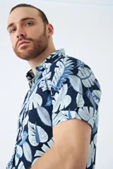 Camisa de manga corta con estampado botánico de hojas en tonos azul y blanco. Presenta cuello clásico, cierre frontal abotonado y corte slim.