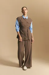 Chaleco negro de corte estructurado con cuello redondo, cierre frontal oculto y lazo ajustable en la cintura. Presenta dos bolsillos frontales con solapa y diseño de hombros caídos.