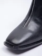 Botín negro de cuero sintético, caña corta, con punta cuadrada y cierre frontal central. Posee un taco bajo y grueso.