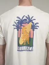Remera color crema de algodón, con cuello redondo y mangas cortas. Estampado en la espalda con diseño de palmeras, tabla de surf y la palabra 'Mallorca'.