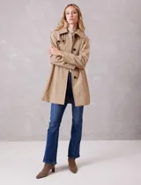 Gabardina trench de tejido repelente al agua en color beige. Presenta cuello con solapa ancha, cierre frontal con botones en tono carey, capucha desmontable y lazo de ajuste en la cintura. Incluye bolsillos laterales tipo ojal y forro interno a tono.