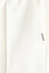 Pantalón tipo jogger de corte sastrero, color blanco, confeccionado en tejido de punto de peso medio. Presenta pliegue cosido frontal, cintura elástica con cordón de ajuste, bolsillos laterales y bolsillo trasero insertado.