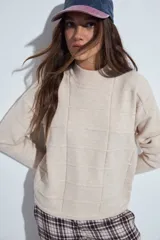 Sweater de punto color beige con cuello a la base y diseño de trama geométrica en relieve. Presenta un calce relajado, mangas largas y puños tejidos.