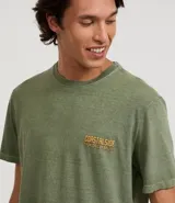 Remera de hombre, modelo comfort, color verde oliva desteñido, con cuello redondo y manga corta. Presenta un pequeño estampado en el pecho con lettering en tonos naranjas que dice "COASTALSIDE".