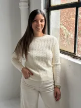 Sweater de punto color crudo con diseño de trenzas verticales, cuello redondo y mangas largas.
