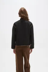 Chaqueta negra de poliéster con cuello a la base, cierre frontal con botones y dos bolsillos delanteros. Presenta detalles de bordado decorativo en color marrón en los bordes, cuello, puños y bolsillos.