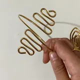 Brazalete dorado de alambre con diseño geométrico en forma de espiral.