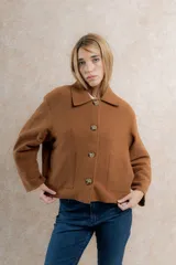 Chaqueta corta tipo blazer color marrón, confeccionada en tela de lana afieltrada. Tiene cuello camisero, silueta cuadrada, cierre frontal con botones y bolsillos delanteros.
