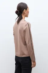 Remera de manga larga color tostado con escote en V y detalles de vivos en contraste color negro que recorren el frente y los laterales de las mangas.