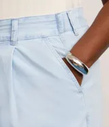 Pantalón tipo pantacourt de jeans en tono delavê, con corte amplio y largo a media pantorrilla. Presenta cintura con elástico en la espalda, cierre frontal con botón forrado, bolsillos laterales tipo cuchillo y pliegues delanteros.