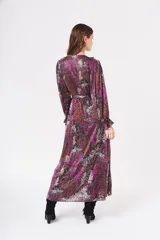 Vestido largo cruzado con estampado floral en tonos fucsia, rojo, blanco y azul sobre fondo negro. Presenta escote en V, cuello con volados y mangas largas abullonadas con puños elásticos. Incluye un lazo para ajustar en la cintura.