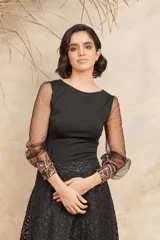 Blusa negra con cuerpo ajustado y mangas largas de tul transparente con puños decorados con lentejuelas.