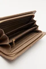 Billetera de mano con textura efecto cocodrilo, color beige, con cierre perimetral y tira de muñeca desmontable.