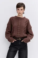 Sweater de punto color blanco off-white, con cuello redondo y diseño texturizado con trenzas y pompones en el frente.