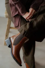 Botín negro de charol con punta cuadrada y hebilla metálica decorativa.