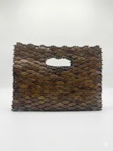 Cartera de mano estructurada, completamente revestida con pequeñas piezas de madera en forma de hoja dispuestas en patrón de escamas, con manija integrada y cierre superior.