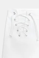 Shorts mini de tiro bajo color blanco, con detalles de cordones cruzados en los laterales delanteros y bolsillos de plastrón en la espalda. Con cierre frontal con cremallera y gancho metálico.