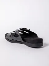 Sandalia baja negra con textura de cocodrilo (croco) en las tiras anchas. Presenta dos hebillas metálicas plateadas ajustables. La base es negra y plana.