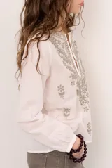 Blusa celeste de manga larga con delicados bordados florales en tono más claro en la zona del pecho y mangas. Presenta escote en V y puños elásticos abotonados.