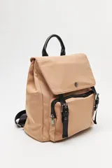 Mochila urbana de nylon color beige, con solapa superior, bolsillo frontal con cierre y correas decorativas con hebillas metálicas. Incluye manija superior y correas ajustables.
