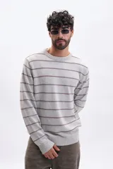 Buzo de tejido de punto en color gris melange, con diseño de rayas horizontales finas en color bordó. Presenta cuello redondo y puños y ruedo acanalados.