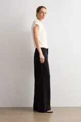 Pantalón de corte recto y tiro medio, confeccionado en tejido negro de textura sutil. Presenta un diseño minimalista con cierre frontal oculto y caída fluida.