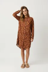 Vestido camisero de manga larga, color marrón con estampado abstracto en tonos más claros. Tiene cuello de camisa y cierre frontal con botones blancos.