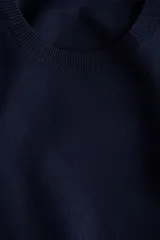 Buzo de punto suave en color azul marino, con cuello redondo, mangas largas abullonadas con frunces en los hombros y terminaciones acanaladas en cuello, puños y bajo.