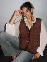 Chaleco tejido color tostado con destellos de lurex, escote en V y cierre frontal con botones. Presenta detalles de bordados y terminaciones en crochet en color crudo.
