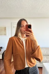 Camisa de gamuza color cognac con cuello redondo, cierre frontal abierto y bolsillos frontales tipo parche. Presenta mangas largas con puños ligeramente acampanados y un corte recto.
